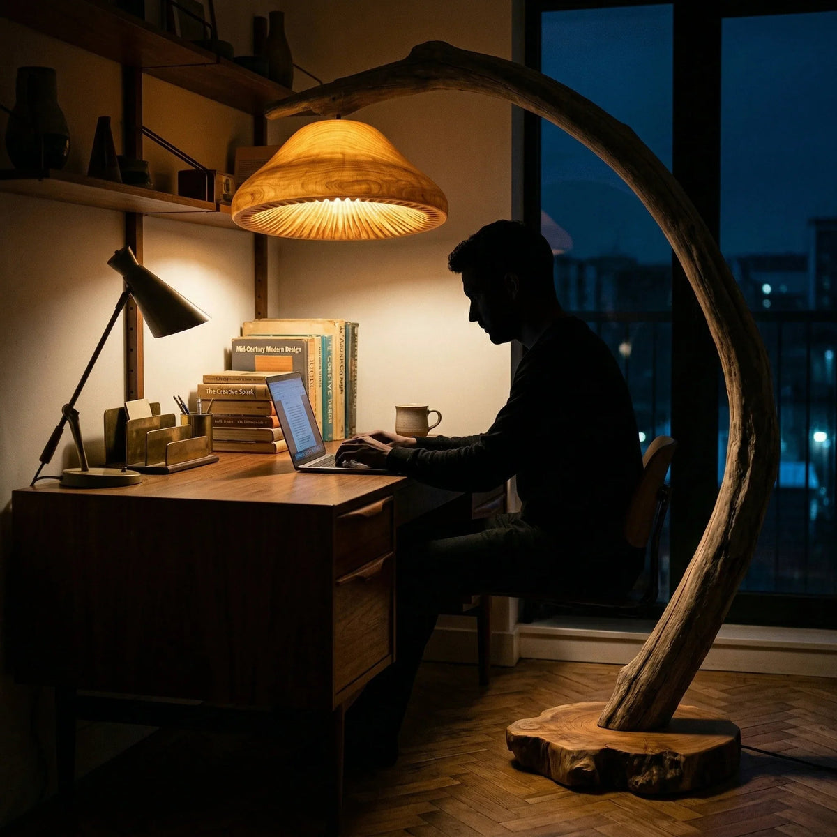 Mann arbeitet an einem Holzschreibtisch, beleuchtet von einer Baumkanten-Treibholz-Pilz-Stehlampe