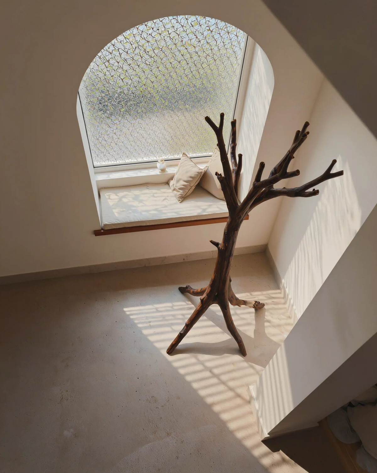 Baum-Bücherregal aus Massivholz in einem minimalistischen Raum neben einer gewölbten Fenstersitzbank mit Kissen