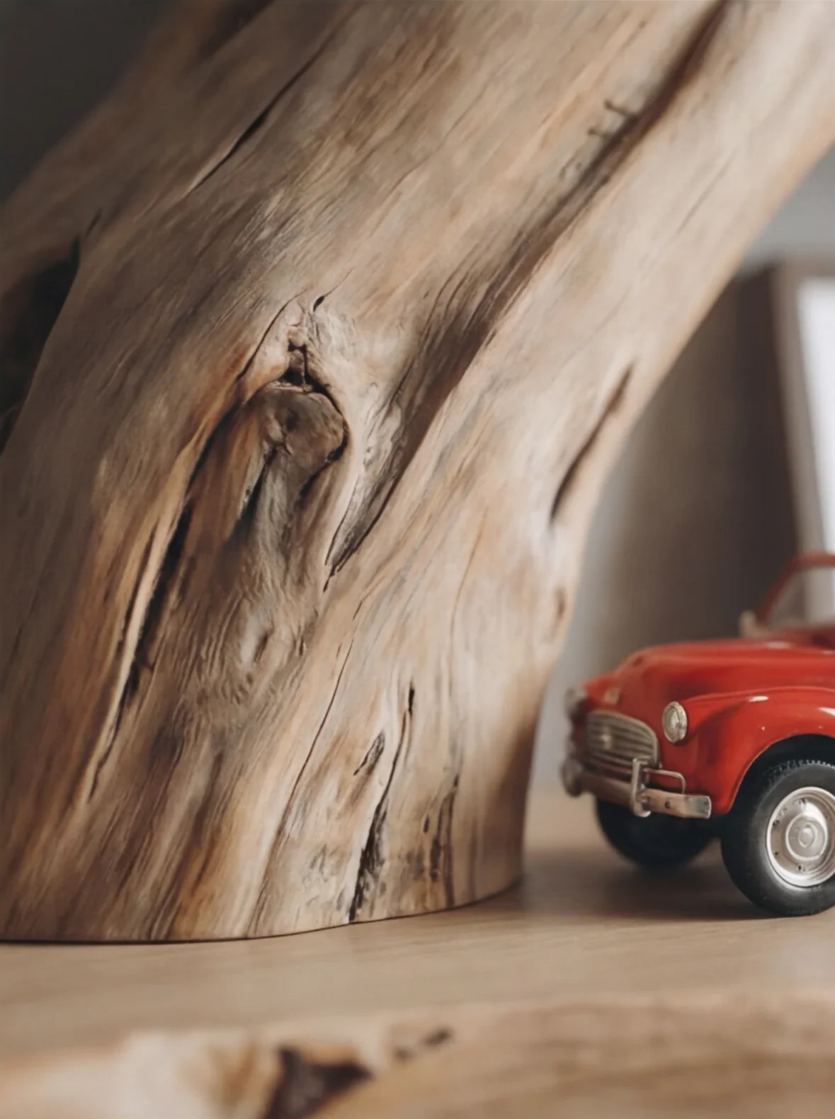 Nahaufnahme eines Massivholzmöbels mit natürlicher Baumkante und einem kleinen roten Spielzeugauto daneben.