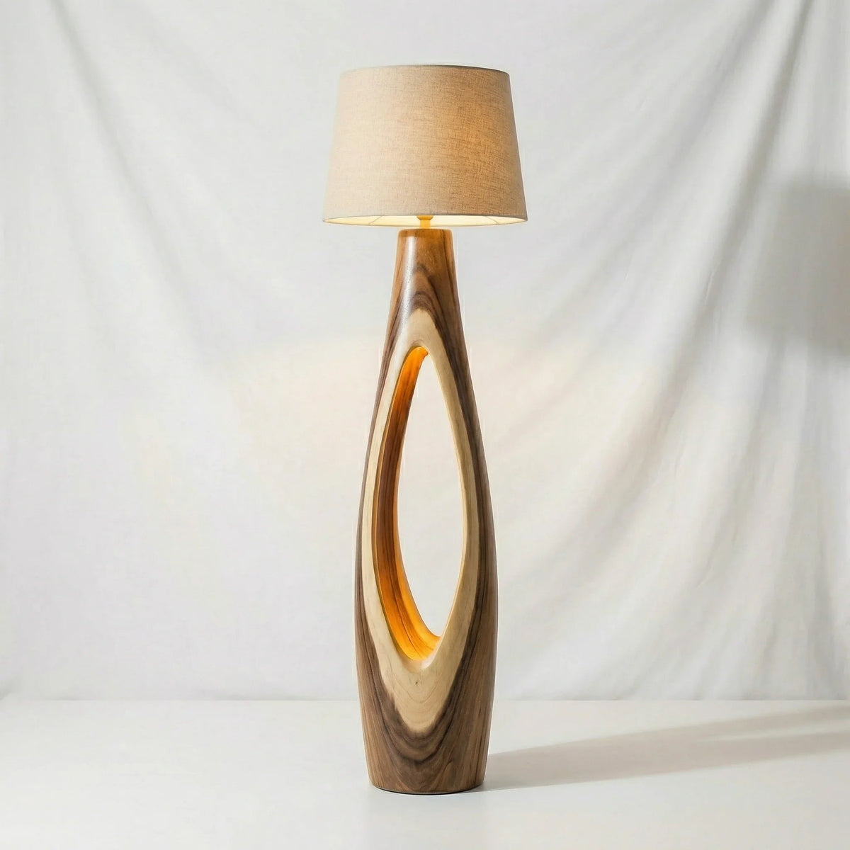 Moderne Stehlampe mit ovalem Massivholzfuß und beigem Stoffschirm vor weißem Hintergrund